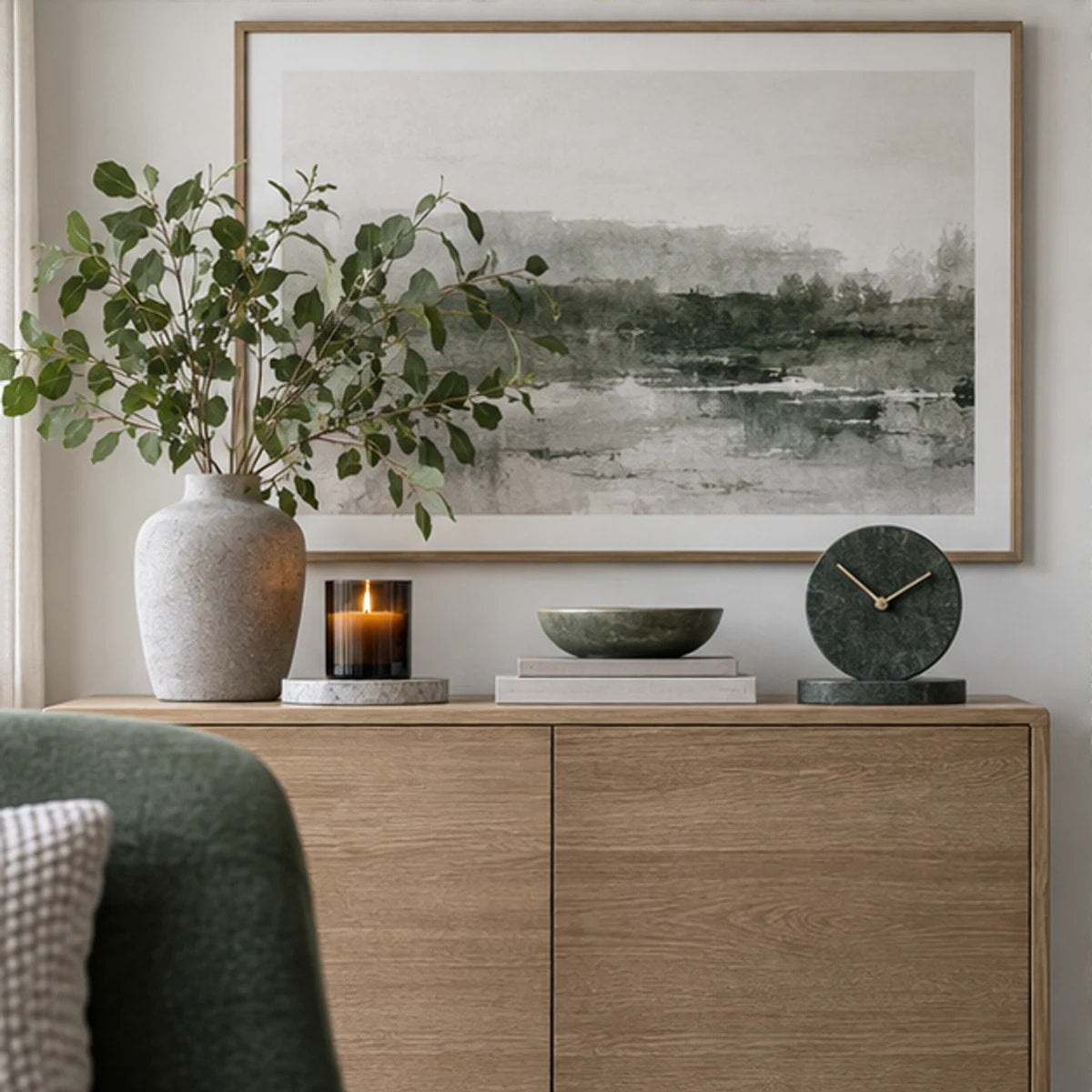 A styled home decor console with art, candle, vase and clock